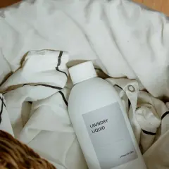Botella de detergente para ropa en una cesta con ropa de lino. Aprende como lavar el lino para que no encoja.