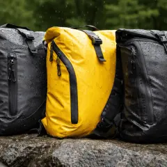 Tres mochilas, una amarilla y dos negras, con tejido impermeable Gore-Tex, mojadas por la lluvia sobre rocas.