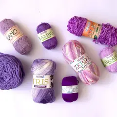 Ovillos de lana y acrílico en tonos morados y rosados, listos para tejer prendas de abrigo y accesorios.