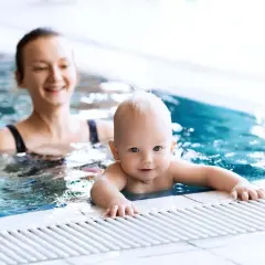 Un bebé sonriente disfruta de la natación con su madre en una piscina.