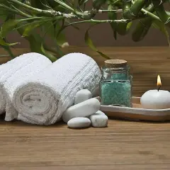 Toallas blancas enrolladas, sales de baño azules, vela encendida y bambú, ideal para recuperar toallas ásperas y disfrutar de un momento de spa.