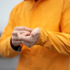 Persona ajustando la manga de su chaqueta naranja de poliéster.