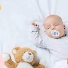Bebé de 4 meses duerme de lado con chupete y osito.
