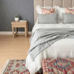 Cama acogedora con colcha de lino que da calor. Cojines grises y alfombra de estilo étnico.