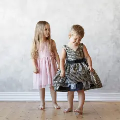 Dos niñas, una con un vestido rosa y otra con uno dorado y negro, muestran la ropa que llevan los niños en una boda.