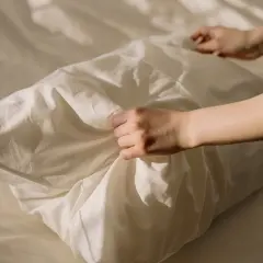 Manos arreglando una funda de almohada blanca, como si se preparara para blanquear fundas de almohadas amarillentas.
