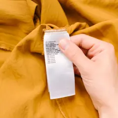 Etiqueta de cuidado de una prenda de color mostaza. Indica "100% viscosa", advirtiendo que la viscosa encoge si no se cuida.
