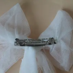 Un delicado lazo de tul blanco, adornado con perlas, sujeto por una pinza plateada.