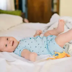 Mi bebé de 2 meses se voltea, sonriendo y jugando con un dinosaurio de juguete en la cama.