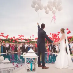 Novios liberando globos en una boda, rodeados de invitados y niños.