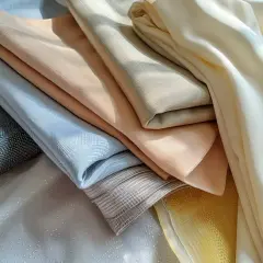 Apilamiento de telas de poliéster o microfibra en tonos pastel y neutros, con texturas sutiles y pliegues suaves.