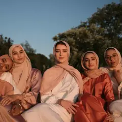 Seis mujeres con hiyabs posan juntas. El tejido modal se arruga suavemente en sus vestidos, creando un efecto elegante bajo la luz del atardecer.