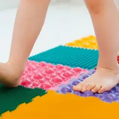 Niño camina sobre un tapete terapéutico de colores para fortalecer sus pies planos.