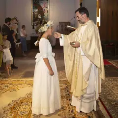 Niña recibe la comunión, un momento especial que marca a qué edad se hace la comunión. Familiares observan.