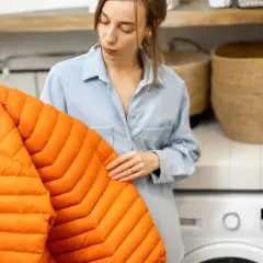 Mujer revisa un abrigo naranja, pensando cómo secar un plumas sin secadora.