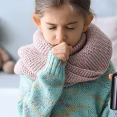 Niña con tos y bufanda, sosteniendo un frasco de medicina. Una imagen que ilustra cómo calmar la tos en niños.