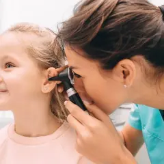 Médico examina el oído de una niña con otoscopio. Una revisión para descartar otitis en niños.