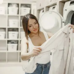 Mujer saca ropa de la secadora de lino. Estantes con cestas blancas al fondo.