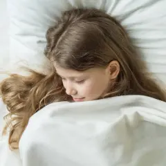 Niña rubia duerme acurrucada, quizás soñando con terrores nocturnos. Su cabello se esparce sobre la almohada blanca.