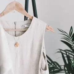 Vestido de lino beige colgado en percha, con collar dorado. Descubre trucos para que no se arrugue el lino y mantén tu ropa impecable.