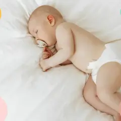 Un tierno bebé duerme de lado, con un chupete en la boca, envuelto en una suave manta blanca.
