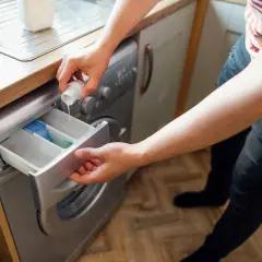 Persona vierte detergente en la lavadora para que la ropa acartonada quede limpia y suave.