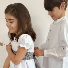 Hermanos de comunión, un niño ayuda a su hermana a ajustar el lazo de su vestido blanco, preparándose para un día especial.