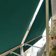 La lona verde protege del sol en un balcón con ladrillos.