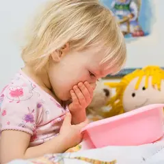 Niña rubia con vómito, posiblemente por rotavirus en niños. Sostiene un recipiente rosa.