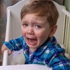 Un niño pequeño con pijama a cuadros azules llora desconsoladamente en su cuna. Mi bebé llora con mucha rabia, con lágrimas corriendo por sus mejillas.