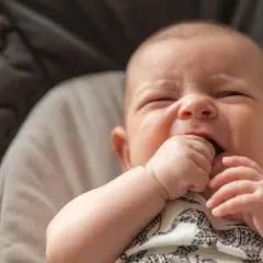 Un bebé de 3 meses intenta incorporarse, con su mano en la boca, en una hamaca acolchada.