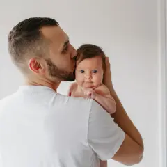 Un padre besa la cabeza de su bebé, que mira a la cámara con sus grandes ojos azules.