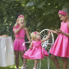 Niñas con vestidos fucsia, una con un fajín para vestido niña, disfrutan de un té en el jardín.