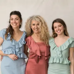 Tres mujeres sonríen, vestidas con trajes elegantes. Ideas para como vestir para un bautizo en invierno.