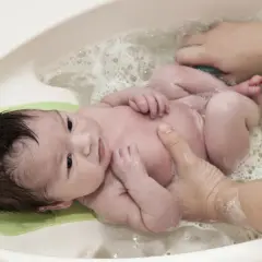 Un bebé sonriente disfruta de su primer baño. Aprende cuando bañar a un recién nacido con este tierno momento.