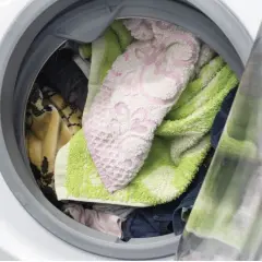 Interior de lavadora con ropa variada: toallas verdes y rosas, mantas y prendas oscuras. ¿Cuánto tiempo puede estar la ropa en la lavadora?