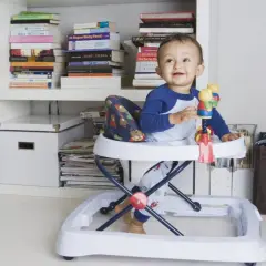 Bebé sonriente en andador, rodeado de libros. Posibles consecuencias del uso del andador en bebés.