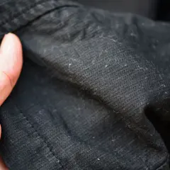 Dedos señalan motas negras en ropa oscura, resultado de la lavadora.
