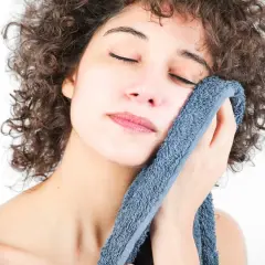 Mujer con rizos oscuros se seca la cara con toallas suaves y con buen olor, disfrutando de un momento de frescura.