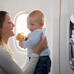Madre sonríe a su bebé en un avión, jugando con un sonajero. Viajar con bebés puede ser una aventura alegre.