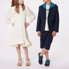 Niño y niña posan con atuendos elegantes. Ideas para como vestir a un niño de 14 años para una boda: traje azul marino con capota y bermudas.