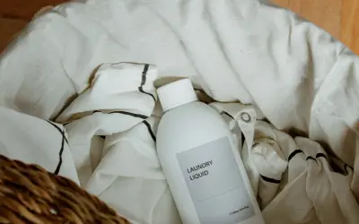 Botella de detergente para ropa en una cesta con ropa de lino. Aprende como lavar el lino para que no encoja.