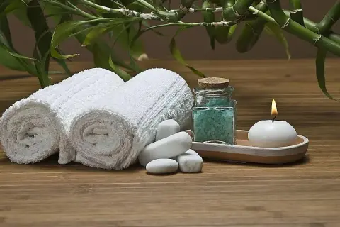 Toallas blancas enrolladas, sales de baño azules, vela encendida y bambú, ideal para recuperar toallas ásperas y disfrutar de un momento de spa.