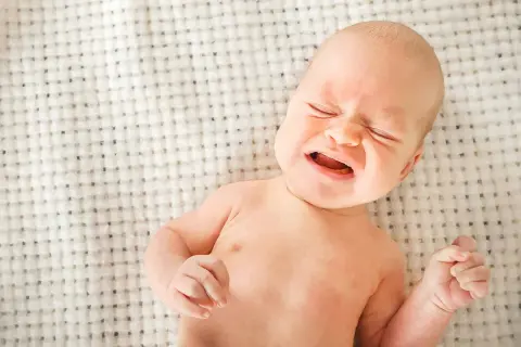 Bebé llorando, con ojos cerrados y boca abierta. Podría ser uno de los signos de deshidratación en bebés.
