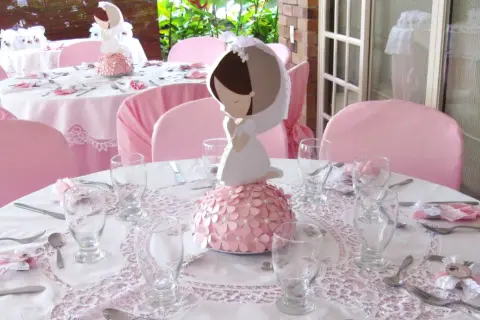 Detalle de decoración comunión niña casera con centros de mesa de comunión y mesas vestidas de rosa.