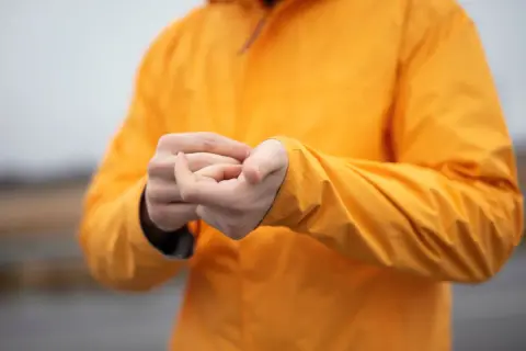 Persona ajustando la manga de su chaqueta naranja de poliéster.
