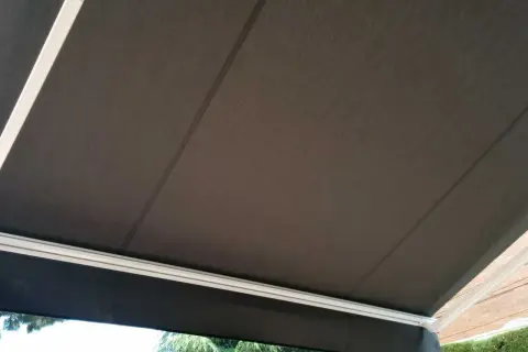 Toldo de acrílico tela oscura, con estructura blanca, protegiendo del sol.