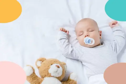 Bebé de 4 meses duerme de lado con chupete y osito.