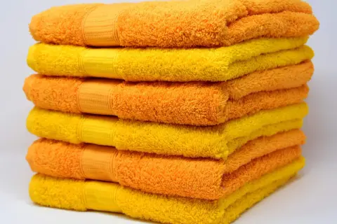 Pila de toallas suaves y esponjosas en tonos naranja y amarillo, listas para un baño reconfortante.