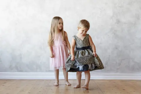 Dos niñas, una con un vestido rosa y otra con uno dorado y negro, muestran la ropa que llevan los niños en una boda.